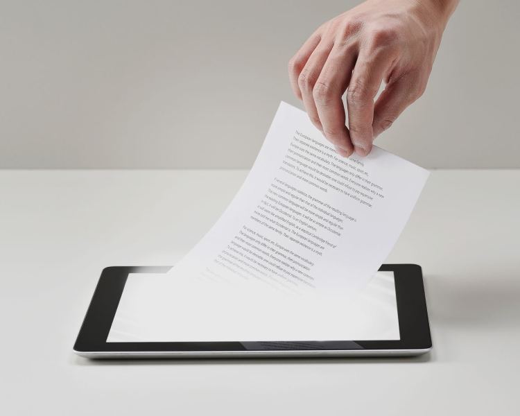 Eine Hand mit einem Blatt Papier über einem Tablet Computer