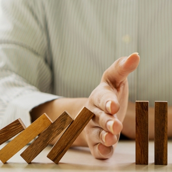 Ein Mann hindert mit seiner Hand Domino Steine daran umzufallen