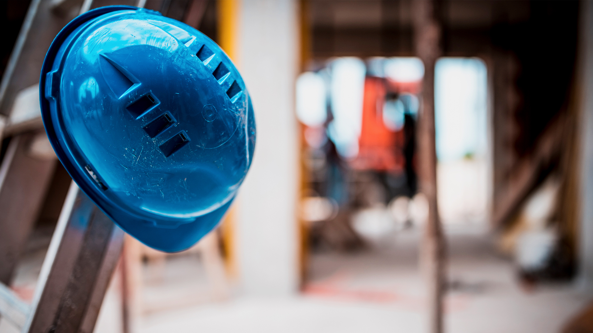 Ein blauer Helm hängt an einer Leiter vor einer Baustelle