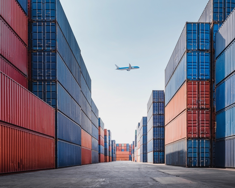 Ein Flugzeug fliegt über Transport-Container eines Frachthafens