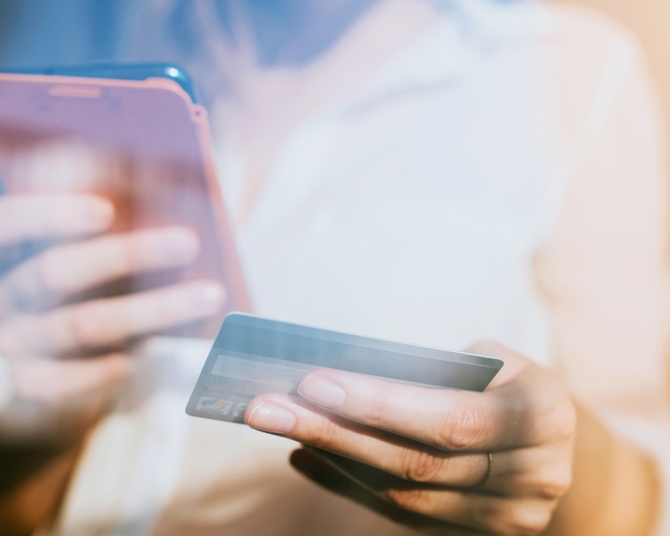 Eine Frau hält in der linken Hand eine Kreditkarte und in der rechten Hand ihr Smartphone