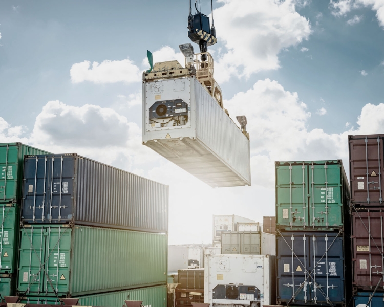Ein Kran befördert einen Transport-Container, darunter stehen weitere Container