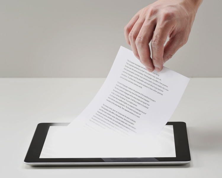 Hand mit Blatt Papier über einem Tablet Computer