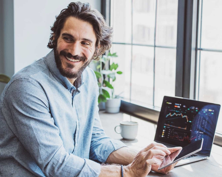 Ein Mann sitzt vor seinem Notebook und tippt auf sein Smartphone