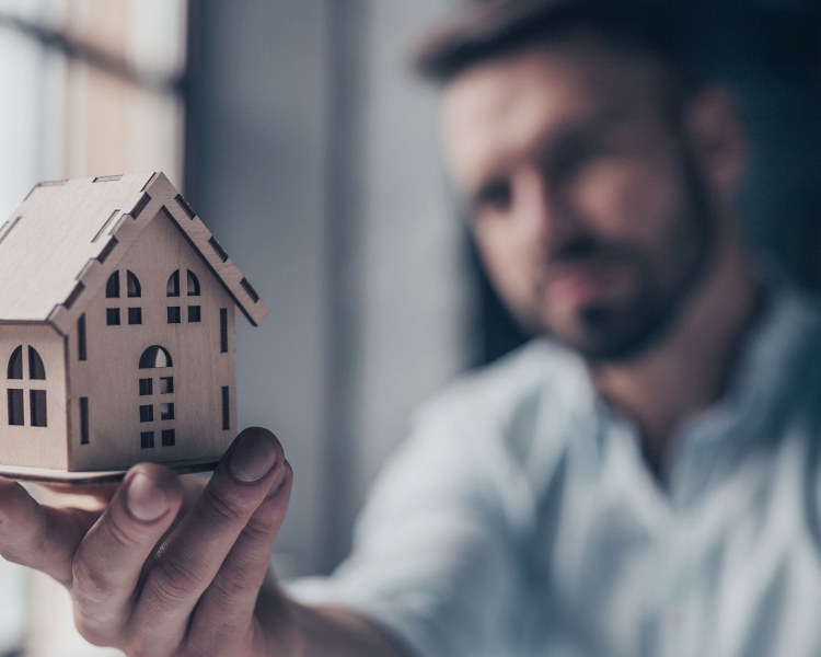 Ein Mann hält ein Modell-Haus in der Hand und blickt darauf