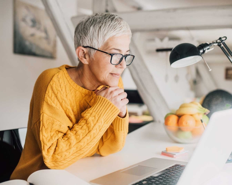 Ältere Dame mit Brille blickt in ihr Notebook