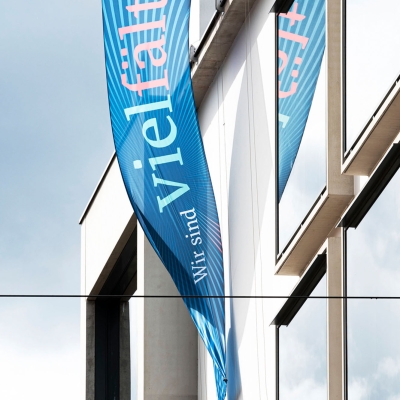 Eine blaue Flagge mit der Aufschrift „Wir sind vielfältig“, die an einem Gebäude befestigt ist.