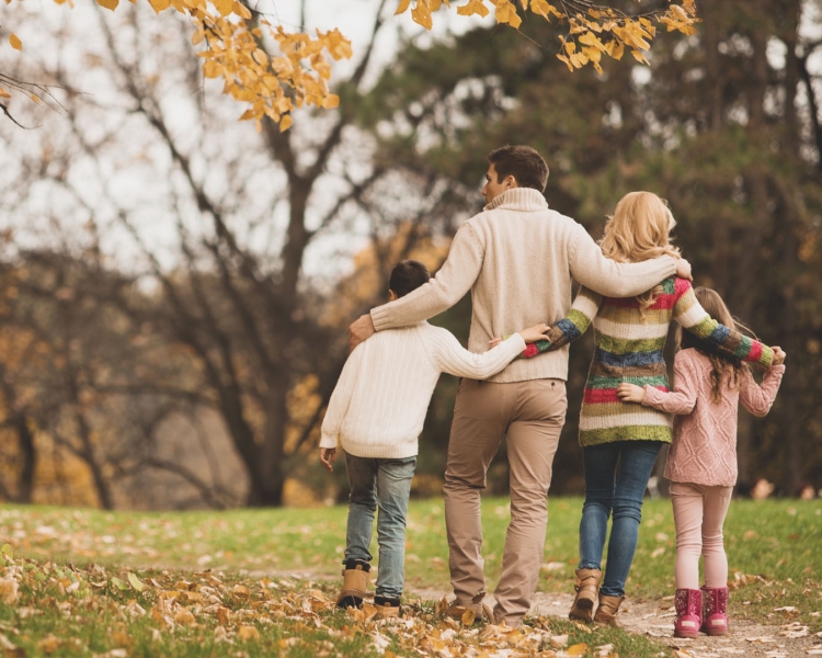 Ein Ehepaar spaziert mit ihren zwei Kindern im Herbst durch einen Park