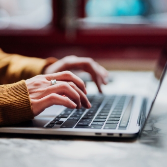 Eine Frau in einem orangen Pulli arbeitet an einem Laptop