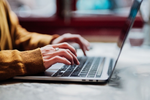 Eine Frau in einem orangen Pulli arbeitet an einem Laptop