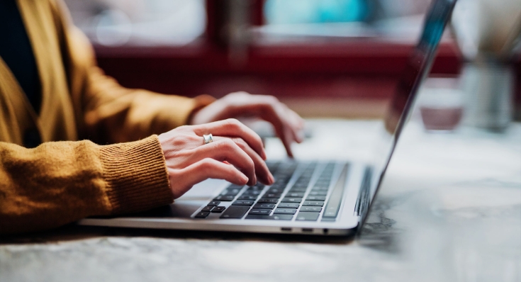 Eine Frau in einem orangen Pulli arbeitet an einem Laptop
