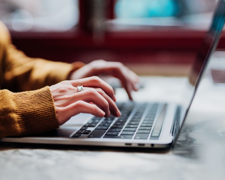 Eine Frau in einem orangen Pulli arbeitet an einem Laptop