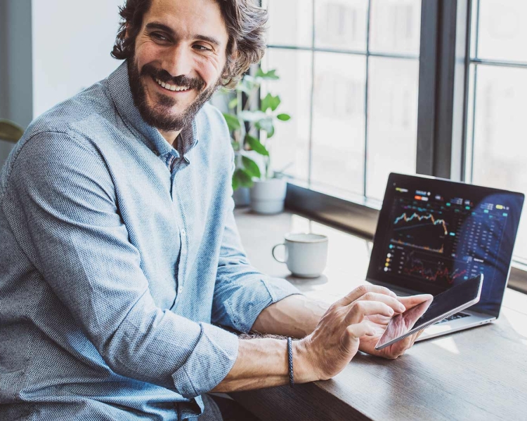 Ein Mann sitzt vor seinem Notebook und tippt auf sein Smartphone