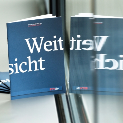 Ein blaues Heft mit der Aufschrift Weitsicht spiegelt sich im Fenster, dahinter liegen weitere Exemplare vom Heft