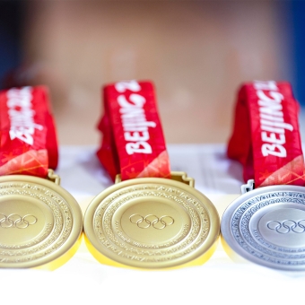 Zwei Goldmedaillen und eine Silbermedaille liegen auf einer weißen Oberfläche