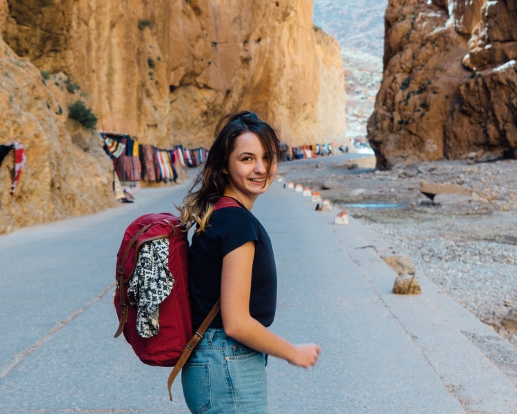 Eine junge Dame ist mit dem Rucksack unterwegs und bewegt sich auf eine Berglandschaft zu