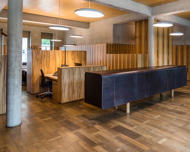 Kanzlei mit Holzboden und langem Tisch in der Mitte sowie mit Schreibtisch im Hintergrund