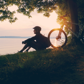 Fahrradfahrer sitzt an einem Ufer eines See's und blickt in die Ferne