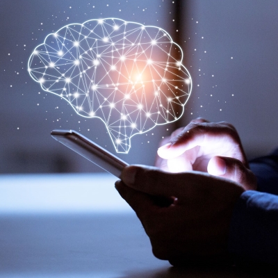 Eine Person tippt auf ihrem Smartphone und über dem Display ist eine Abbildung zusehen, die das neuronale Netzwerk des Gehirns darstellen soll