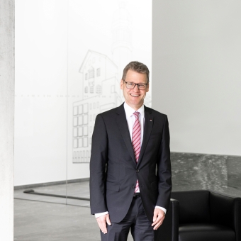 Ein Mann mit einer Brille trägt einen grauen Anzug inklusive rot-weißer Krawatte