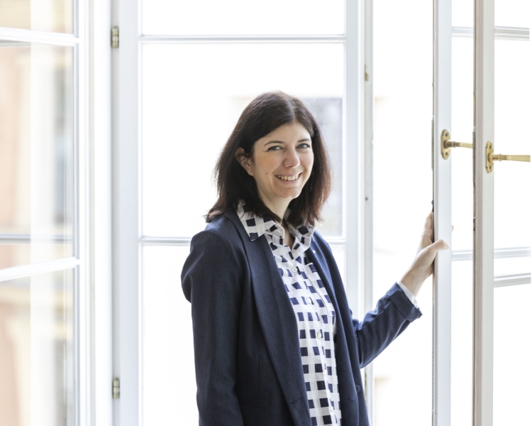 Eine Frau mit schwarzen Haaren steht vor einem Fenster