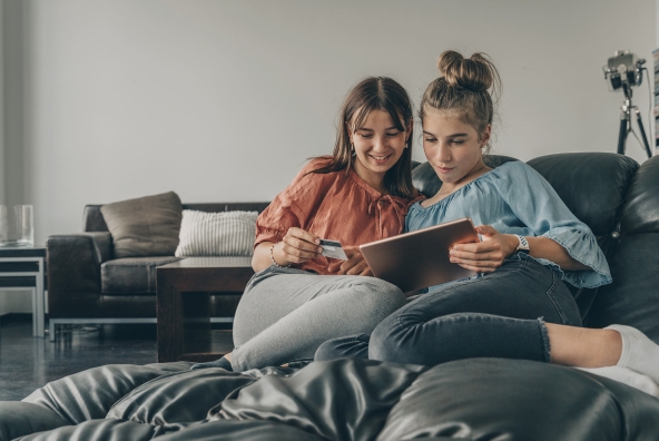 Zwei Freundinnen sitzen auf der Couch und bezahlen mit einer Debitkarte im Internet