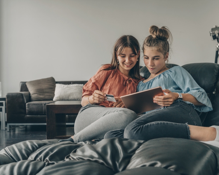 Zwei Freundinnen sitzen auf der Couch und bezahlen mit einer Debitkarte im Internet