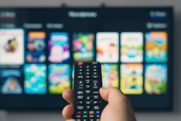 Person hält eine Fernbedienung in der Hand, die Richtung Fernseher gerichtet ist.
