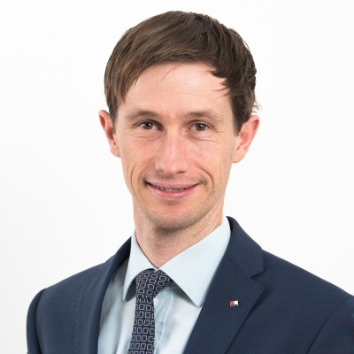 Mag. Martin Mausser trägt einen dunkelblauen Anzug, ein hellblaues Hemd und eine blau gemusterte Krawatte