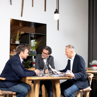Drei Männer unterhalten sich sitzend an einem Tisch.