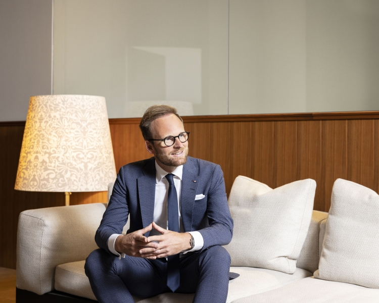 Ein Mann im einem blauen Anzug sitzt auf einer weißen Couch.