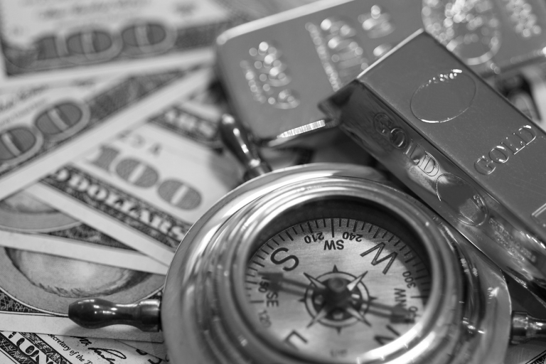 Ein antiker Kompass liegt auf Dollar-Scheinen, daneben befinden sich Goldbarren