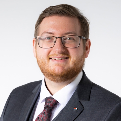 Daniel Neumayr mit grauem Anzug weißem Hemd und rot-schwarz-grau gemusteter Krawatte