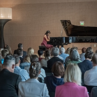 Eine Person spielt auf der Bühne am Klavier, das Publikum blickt auf die Bühne