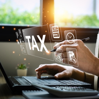 Person an einem Laptop. Über dem Laptop ist das Wort TAX zu sehen.