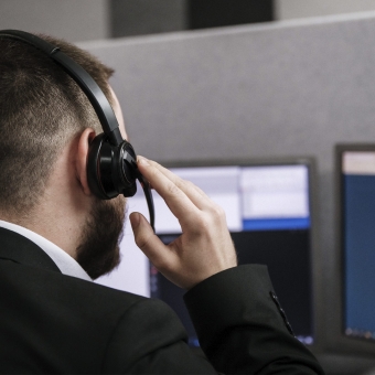 Mann mit Headset telefoniert und sieht auf einen Bildschirm.
