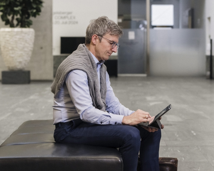 Ein Mann mit einer Brille sitzt auf einem Sessel und arbeitet mit seinem Tablet.