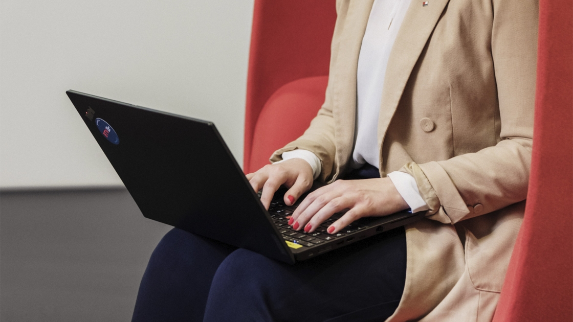 Eine Frau sitzt in einem roten Sessel und und arbeitet mit ihrem Laptop.