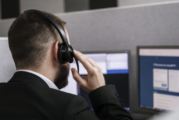 Mann mit Headset telefoniert und sieht auf einen Bildschirm.