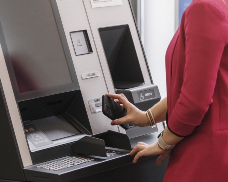 Eine Frau hält ihr Handy an einem Bankomaten.