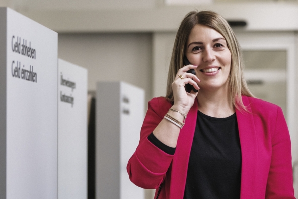 Eine Frau steht neben einem Bankomaten und telefoniert.