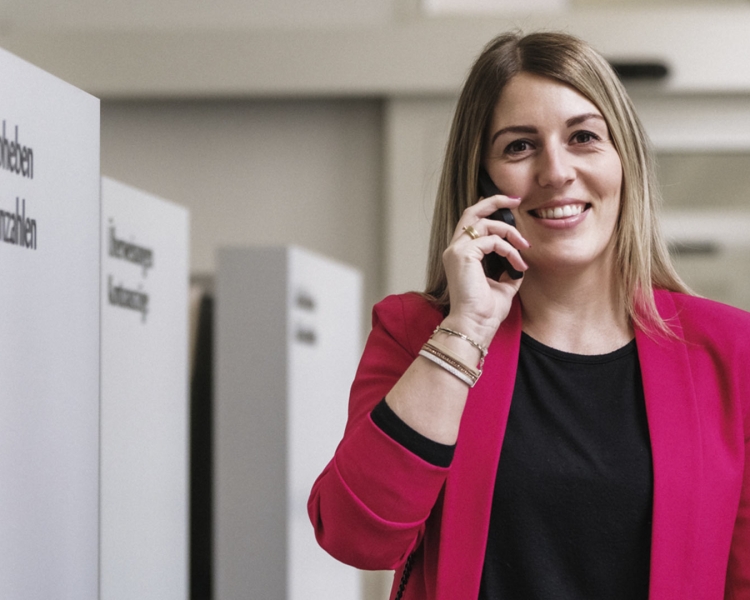 Eine Frau steht neben einem Bankomaten und telefoniert.