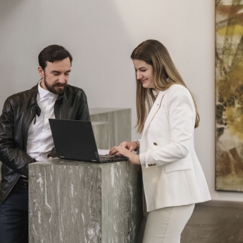 Zwei Personen stehen an einem Stehtisch und nutzen einen Laptop.