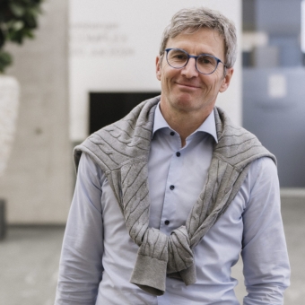 Ein Mann mit Brille und Laptoptasche lächelt ins Bild.