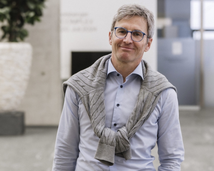 Ein Mann mit Brille und Laptoptasche lächelt ins Bild.