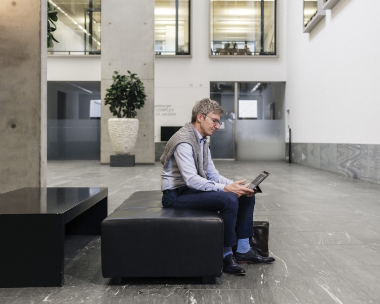 Ein Mann sitzt in einer Lobby und schaut auf sein Tablet