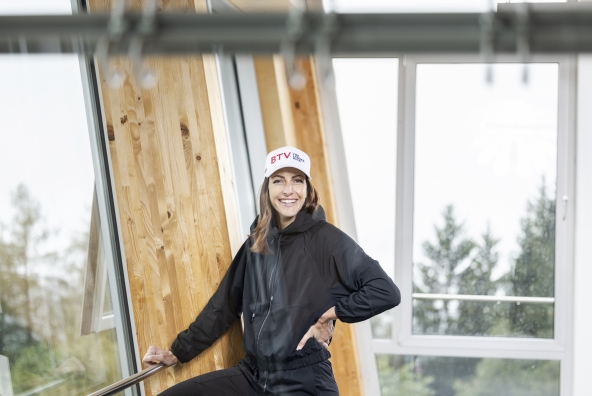 Skeletonfahrerin Janine Flock posiert in einem schwarzen Hoodie vor der Kamera.