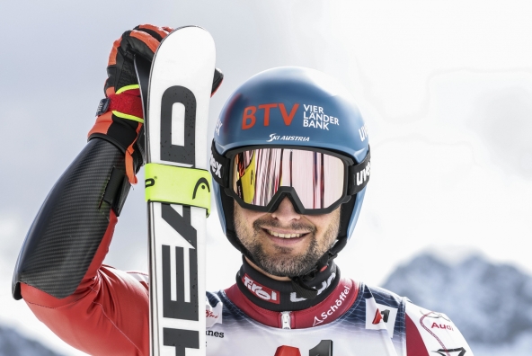 Johannes Strolz in einem Skianzug trägt einen Helm und hält Skier in der Hand.