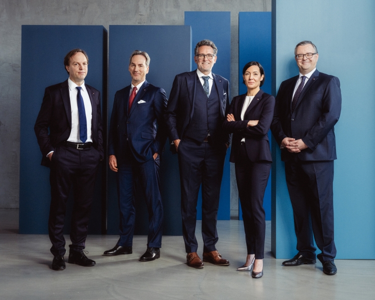 4 Männer und 1 Frau tragen einen Anzug mit einer blauen Wand im Hintergrund.