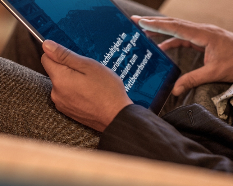 Hände halten ein Tablet in der Hand., auf dem zu lesen ist: Nachhaltigkeit im Tourismus: Vom guten Gewissen zum Wettbewerbsvorteil.